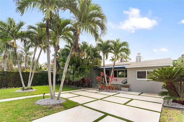 exterior space featuring stucco siding, fence, a patio, a yard, and a chimney