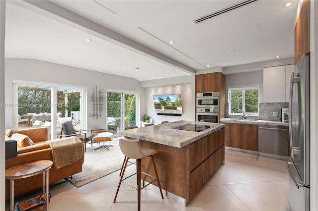 kitchen featuring open floor plan, decorative backsplash, modern cabinets, appliances with stainless steel finishes, and brown cabinets