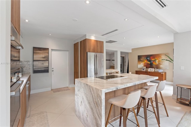 kitchen with black electric stovetop, visible vents, freestanding refrigerator, modern cabinets, and brown cabinets