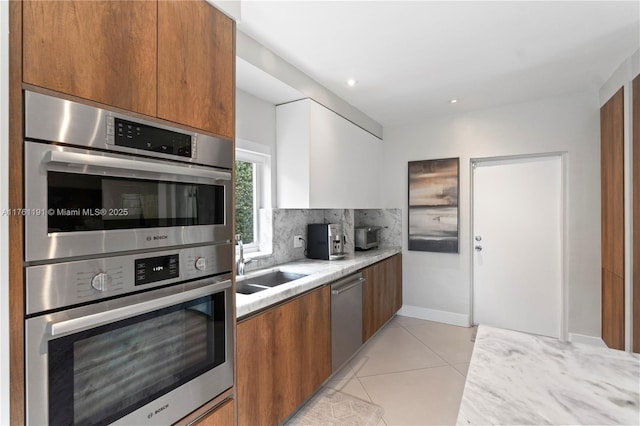 kitchen featuring light tile patterned flooring, light countertops, brown cabinetry, appliances with stainless steel finishes, and backsplash
