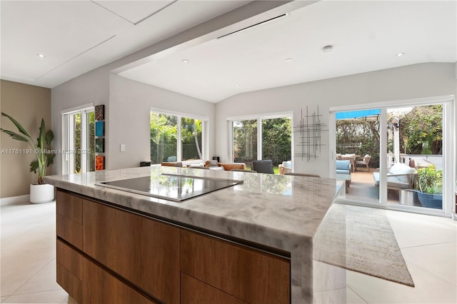 kitchen with light tile patterned flooring, modern cabinets, light stone countertops, black electric stovetop, and a spacious island