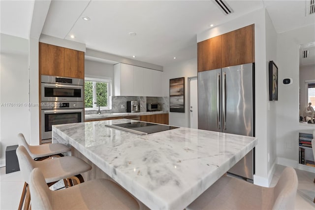 kitchen with modern cabinets, backsplash, brown cabinetry, and appliances with stainless steel finishes