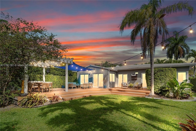 back of house at dusk with a lawn, stucco siding, a deck, and a pergola