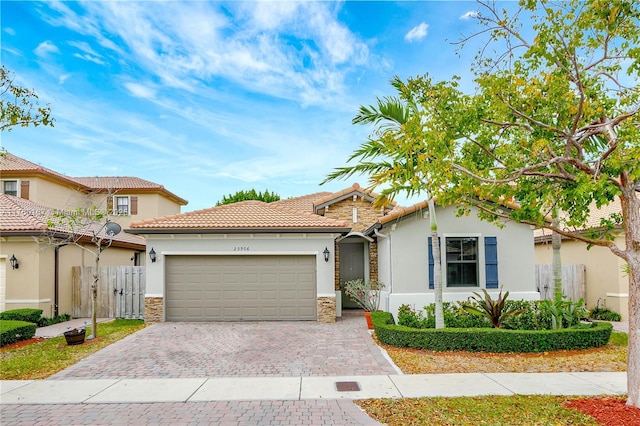 view of front of house featuring stucco siding, decorative driveway, stone siding, a garage, and a tiled roof