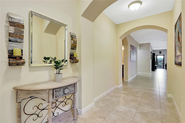 corridor with light tile patterned floors, baseboards, and arched walkways