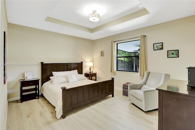 bedroom with baseboards, light wood-style floors, and a tray ceiling