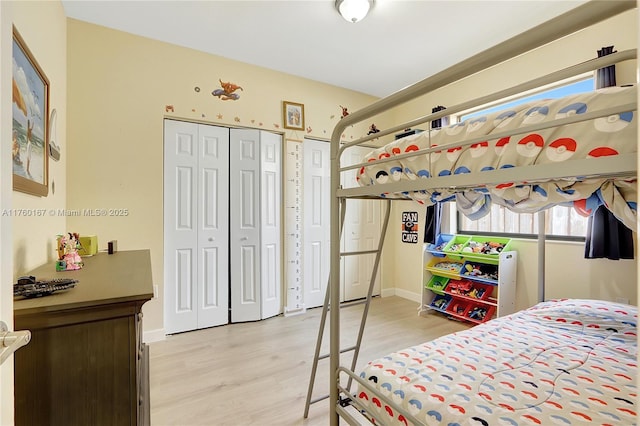 bedroom featuring baseboards, multiple closets, and light wood-style floors