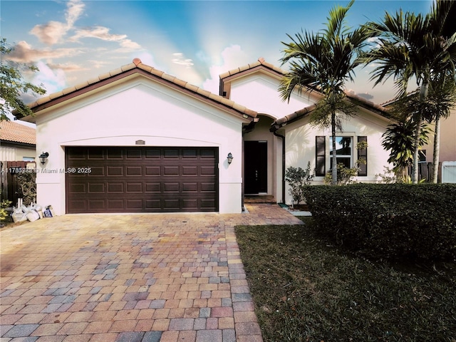view of front of house featuring stucco siding, an attached garage, a tile roof, and driveway