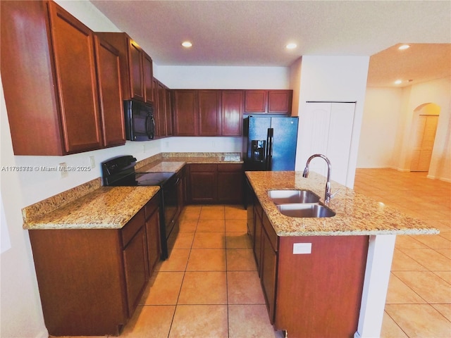 kitchen featuring light tile patterned floors, light stone countertops, an island with sink, a sink, and black appliances