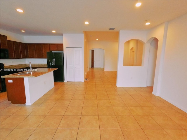 kitchen with a sink, light stone counters, black appliances, and recessed lighting