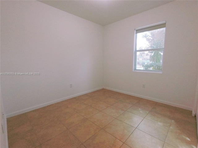 spare room featuring light tile patterned flooring and baseboards