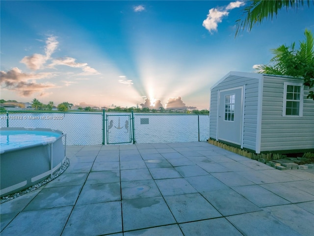 patio terrace at dusk featuring a fenced in pool, fence, an outbuilding, a storage unit, and a gate