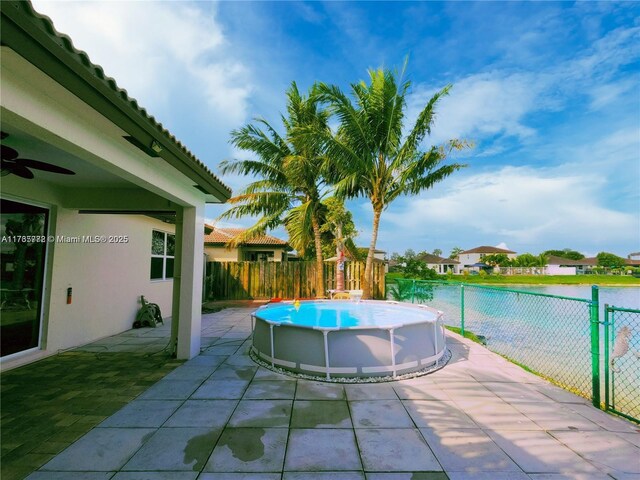 view of pool with a fenced in pool, a fenced backyard, ceiling fan, a water view, and a patio area