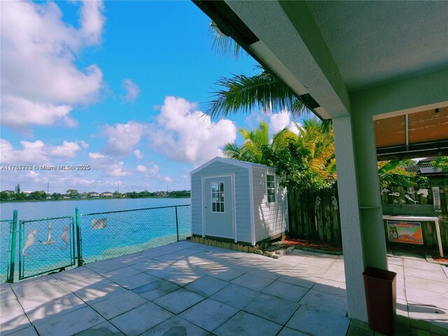 view of patio with a storage unit, a water view, a gate, fence, and an outdoor structure
