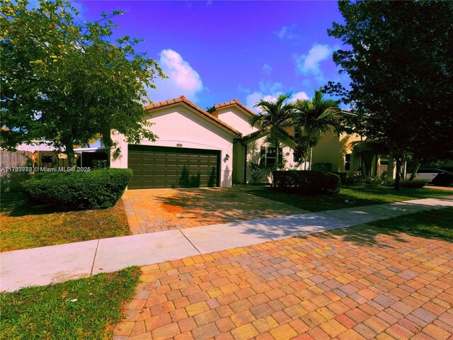mediterranean / spanish-style home with stucco siding, a front lawn, decorative driveway, an attached garage, and a tiled roof