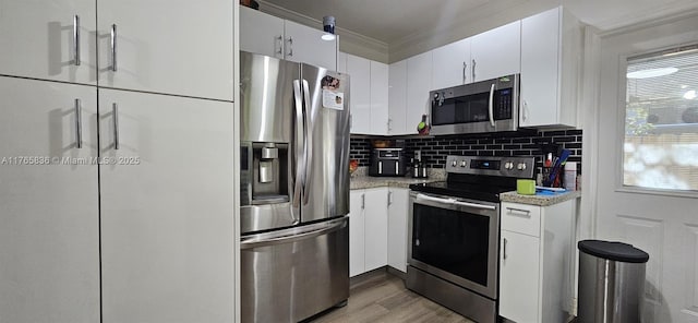 kitchen featuring crown molding, decorative backsplash, wood finished floors, white cabinets, and stainless steel appliances
