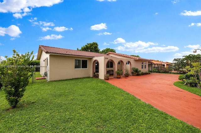 back of house with a tile roof, concrete driveway, stucco siding, fence, and a yard