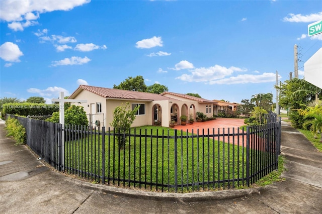 mediterranean / spanish-style home featuring a front lawn, stucco siding, a tiled roof, and a fenced front yard