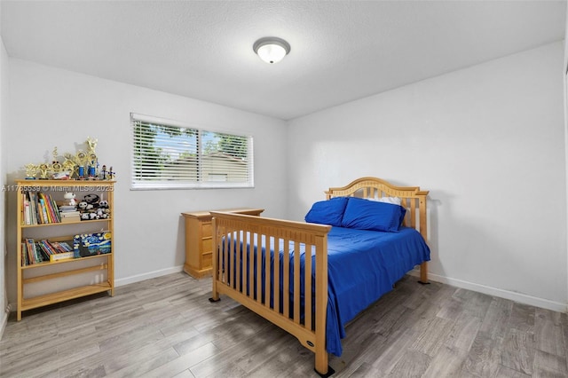 bedroom featuring baseboards, wood finished floors, and a textured ceiling