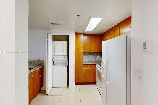 1650 Coral Way Unit Ph-9, Miami, FL 33145 - kitchen with white appliances, stacked washer / dryer, brown cabinetry, light tile patterned floors, and tasteful backsplash