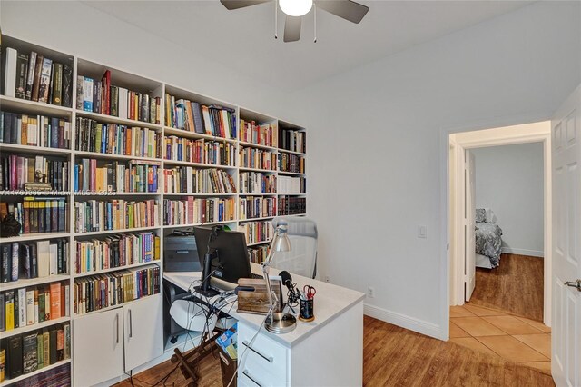 office space with light wood-style floors, a ceiling fan, baseboards, and bookshelves