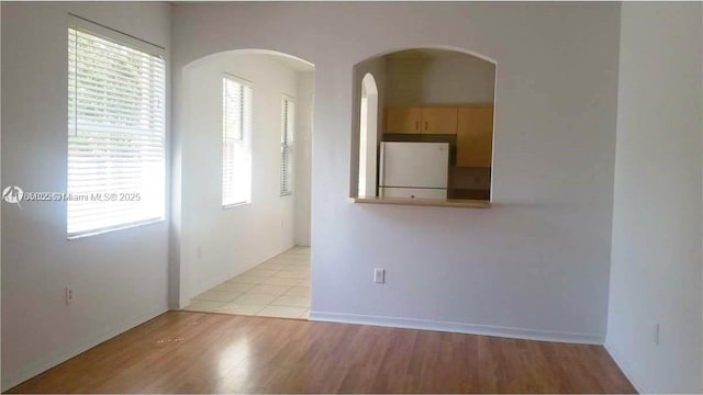 empty room with arched walkways and light wood-type flooring