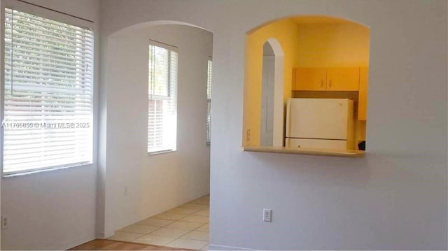empty room with plenty of natural light, arched walkways, and light tile patterned floors