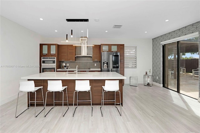 kitchen with visible vents, a large island, wall chimney range hood, appliances with stainless steel finishes, and light countertops