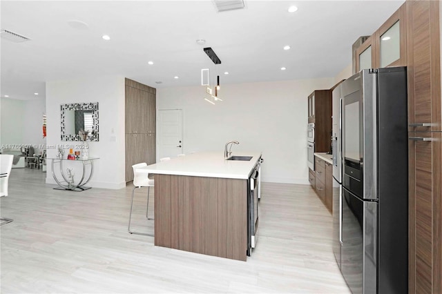 kitchen with a center island with sink, visible vents, a sink, light countertops, and stainless steel refrigerator with ice dispenser
