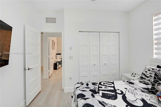 bedroom featuring light wood finished floors, visible vents, baseboards, and a closet