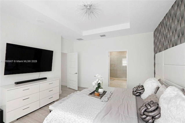 bedroom featuring light wood-type flooring, visible vents, a notable chandelier, connected bathroom, and a raised ceiling