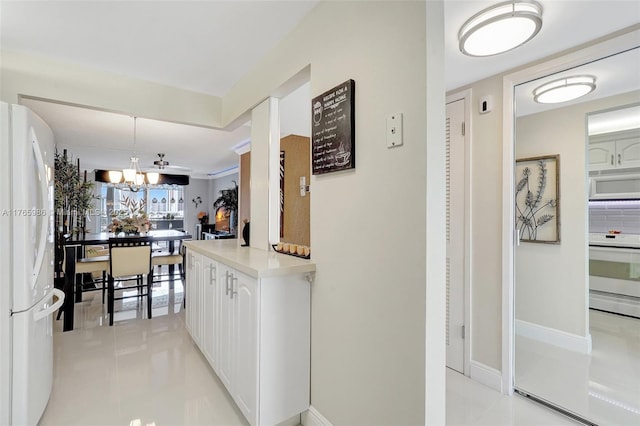 410 Golden Isles Dr Unit 603, Hallandale Beach, FL 33009 - kitchen with a chandelier, light countertops, light tile patterned floors, white cabinets, and white appliances