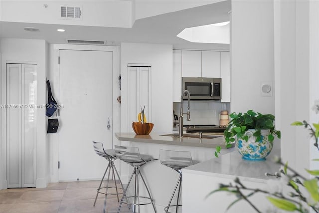 888 Brickell Key Dr Unit 1502, Miami, FL 33131 - kitchen with stainless steel microwave, white cabinetry, a breakfast bar, decorative backsplash, and light countertops