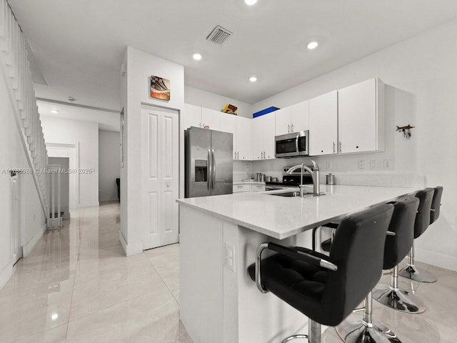 kitchen with visible vents, a peninsula, a sink, stainless steel appliances, and white cabinetry
