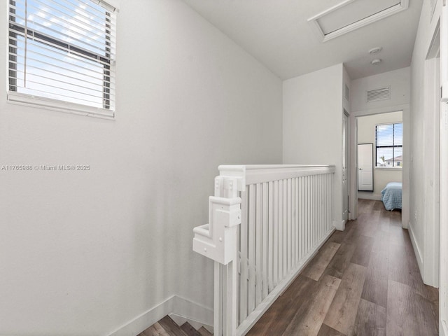 corridor featuring wood finished floors, visible vents, baseboards, attic access, and an upstairs landing