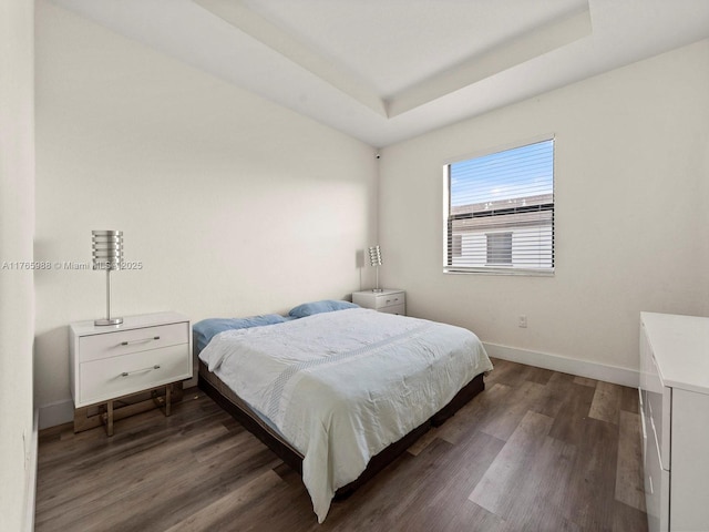 bedroom featuring a tray ceiling, baseboards, and dark wood-style floors