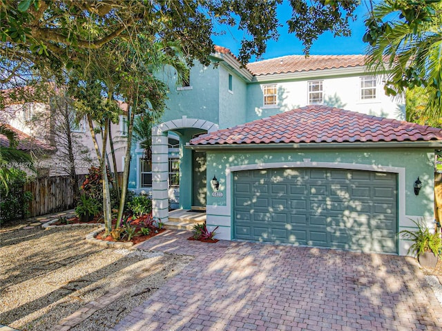 mediterranean / spanish-style home with stucco siding, fence, an attached garage, a tiled roof, and decorative driveway