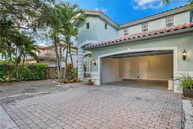 view of front facade with a tiled roof, driveway, stucco siding, and fence