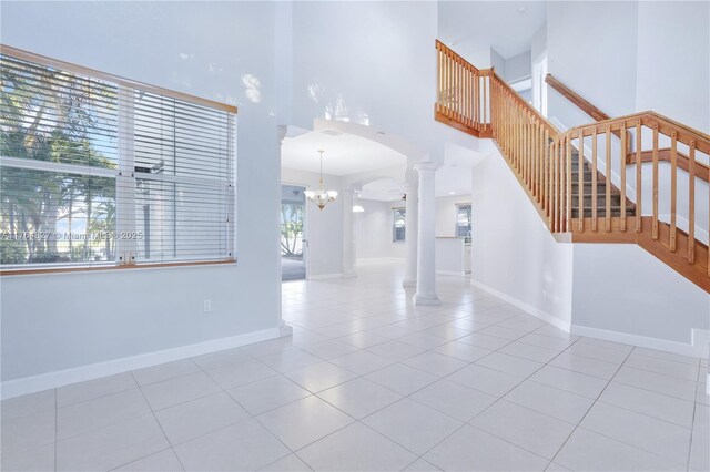 tiled entrance foyer with baseboards, a towering ceiling, decorative columns, arched walkways, and a notable chandelier