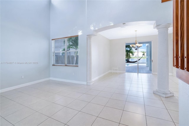 spare room featuring decorative columns, baseboards, a chandelier, light tile patterned flooring, and arched walkways