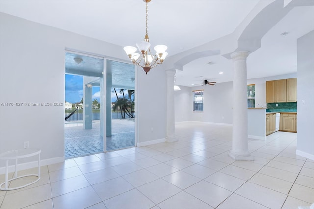 empty room featuring ornate columns, ceiling fan with notable chandelier, baseboards, light tile patterned flooring, and arched walkways