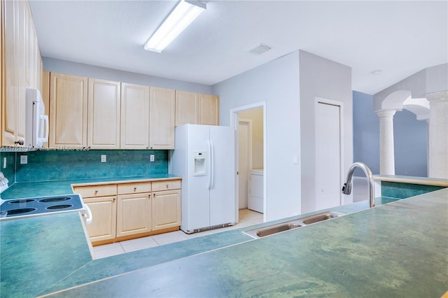 kitchen featuring white appliances, decorative columns, light tile patterned floors, a sink, and washer / dryer
