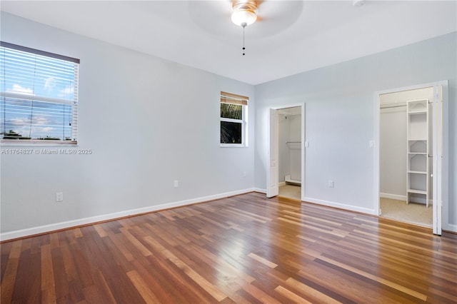 unfurnished bedroom with a walk in closet, baseboards, ceiling fan, and wood finished floors