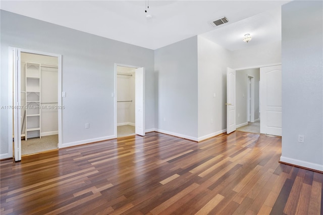 unfurnished bedroom with baseboards, visible vents, a walk in closet, and wood finished floors