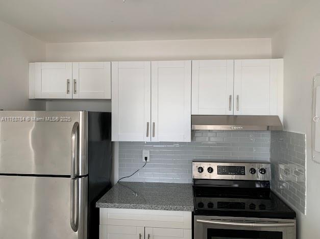 13390 NE 7th Ave Unit 308, North Miami, FL 33161 - kitchen with dark stone counters, stainless steel appliances, under cabinet range hood, white cabinetry, and backsplash
