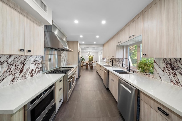 kitchen with a sink, wall chimney exhaust hood, light brown cabinetry, appliances with stainless steel finishes, and modern cabinets
