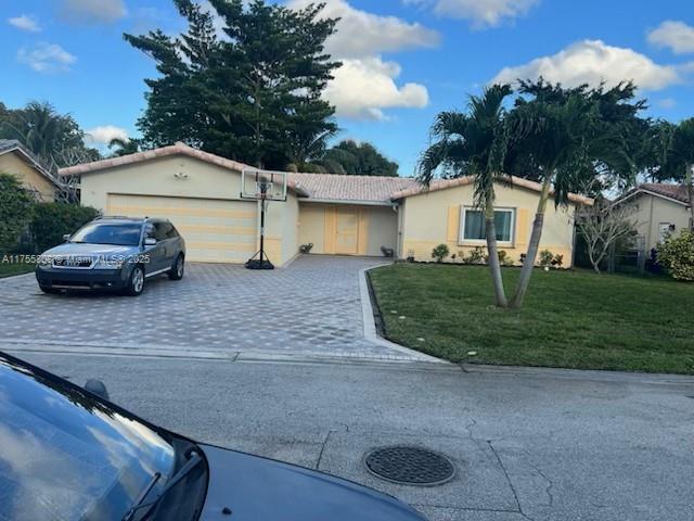 ranch-style home with a garage, stucco siding, driveway, and a front lawn