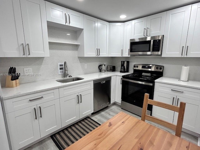 kitchen with a sink, stainless steel appliances, light wood-style floors, white cabinets, and light countertops