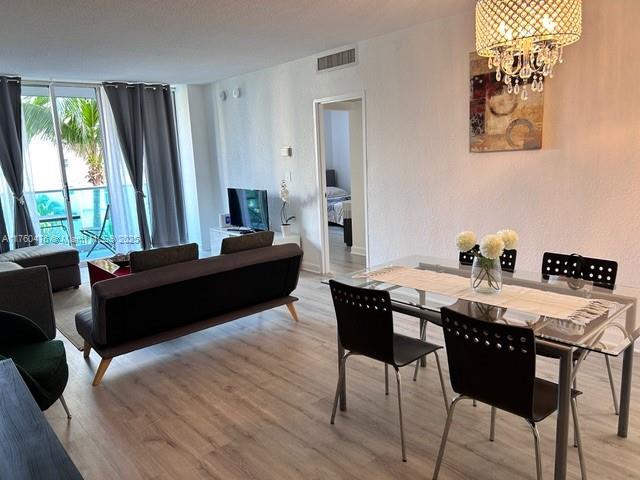 dining space with light wood finished floors, visible vents, a wall of windows, and an inviting chandelier
