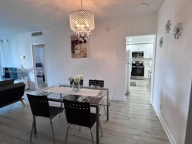 dining room featuring a notable chandelier, light wood-style floors, visible vents, and baseboards
